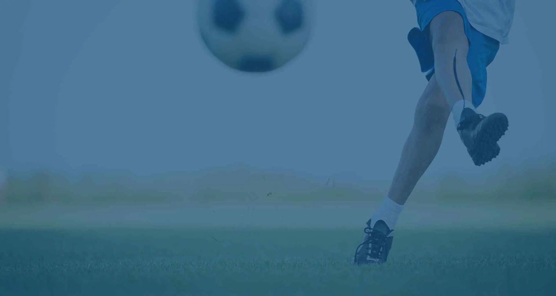 Close-up of a young footballer kicking a ball on grass